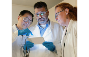 Three doctors in white coats looking at a tablet.